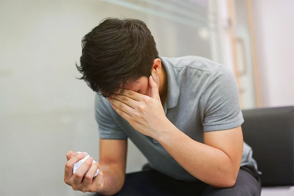 Anxious man sitting on a couch with a tense expression, exploring treatment options like Adderall for anxiety