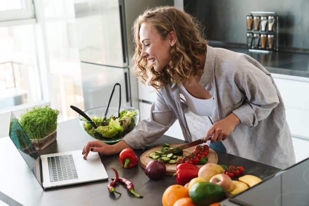 a woman cooking while looking up recipe on her laptop