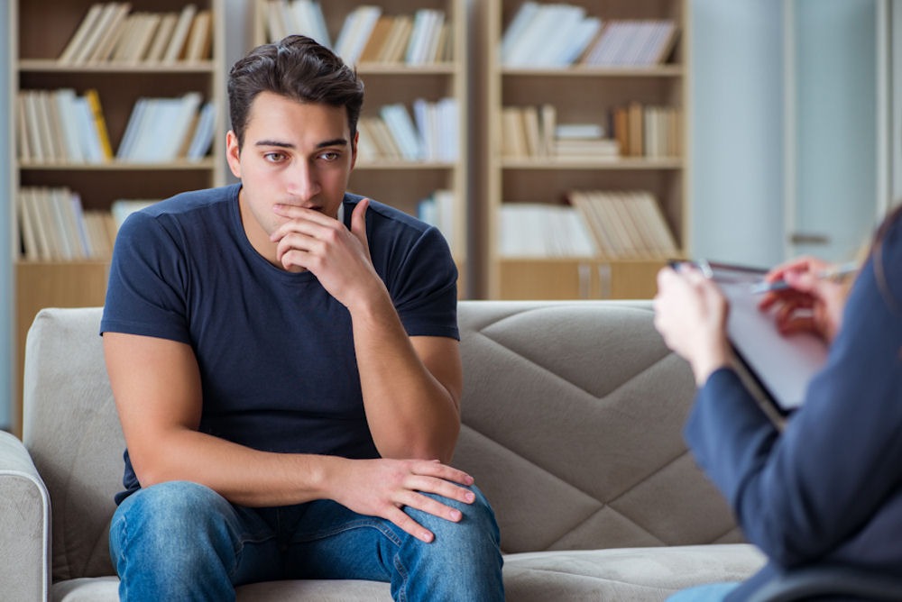 man with hand on mouth sitting in therapy