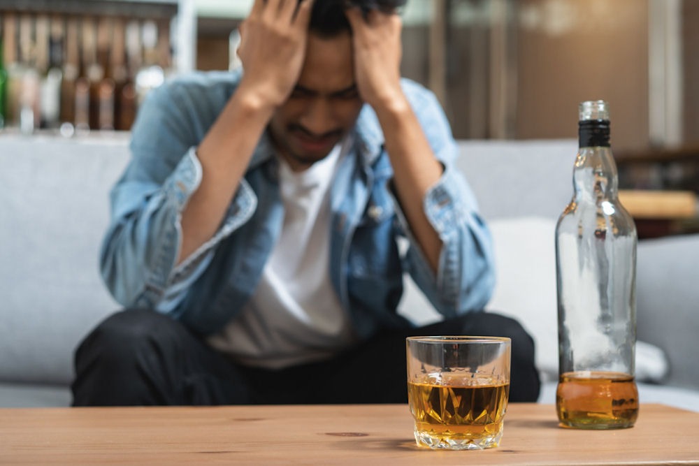 man with hands on head with beer on table