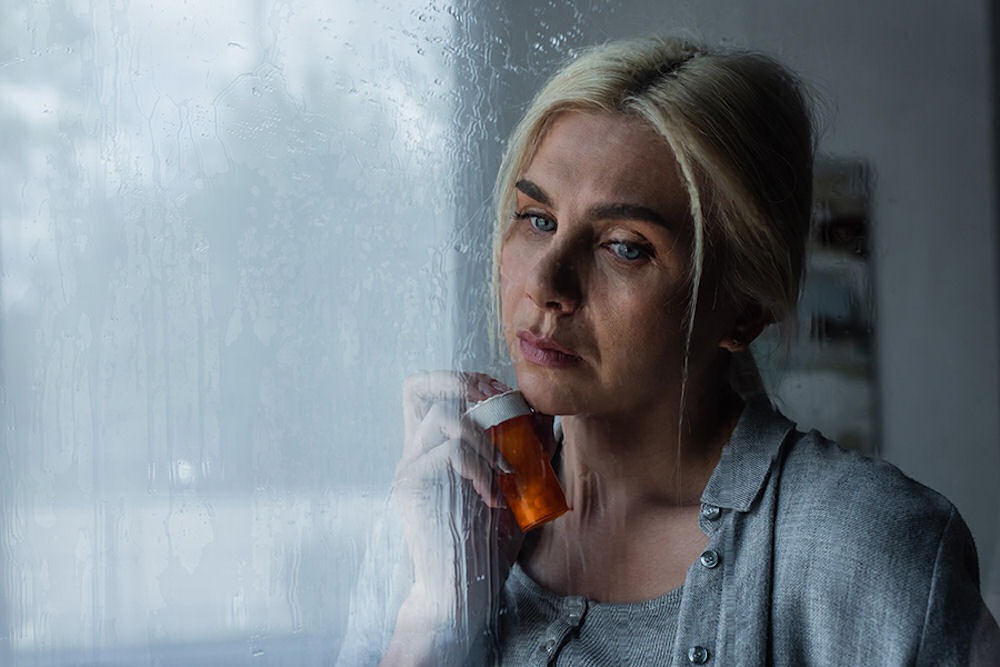 woman-holding-a-bottle-of-pills-staring-out-window