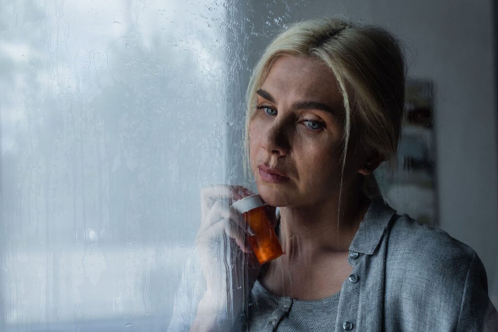 A woman holding a prescription bottle, looking reflective near a rain-streaked window, symbolizing the effects of gabapentin on memory