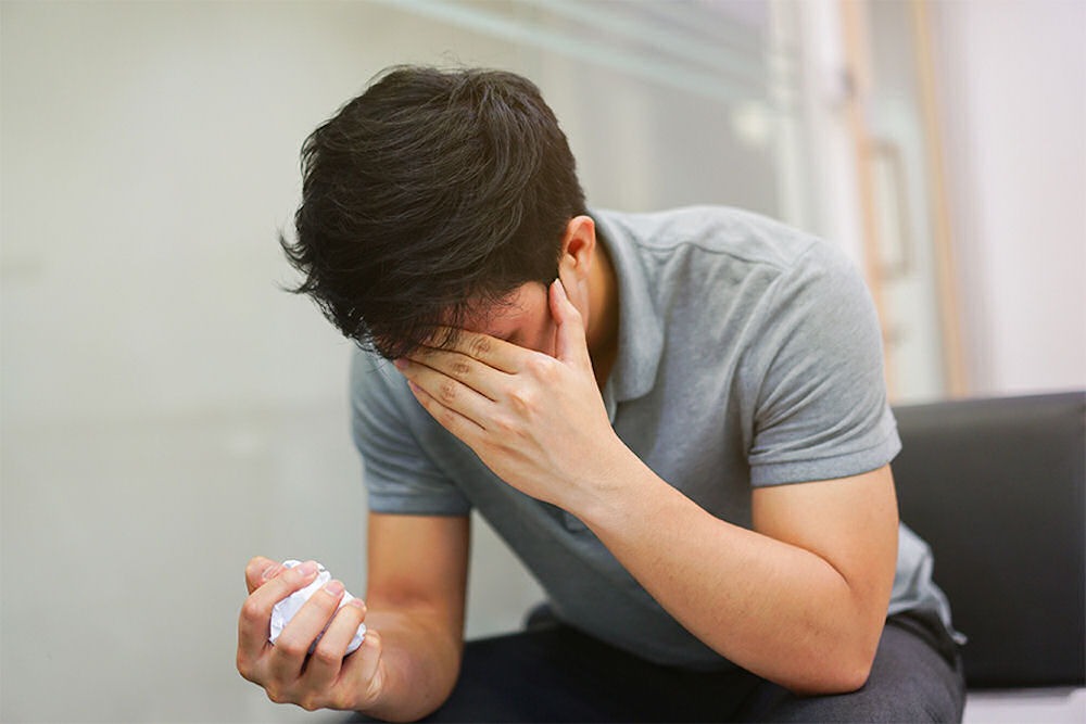 Anxious man sitting on a couch with a tense expression, exploring treatment options like Adderall for anxiety