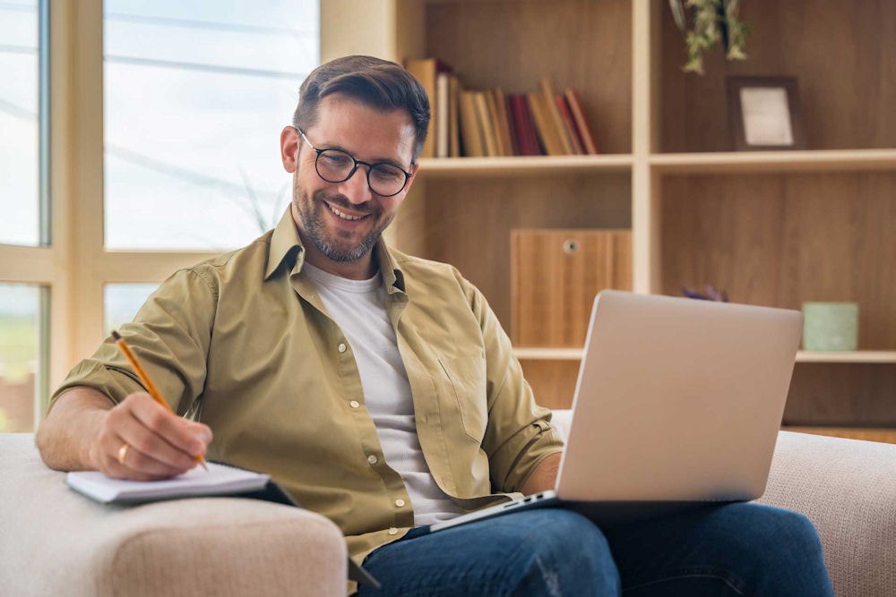 a man smiling and writing while on computer